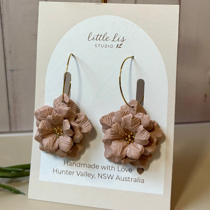 A pair of handmade flower drop earrings by Little Lis Studio, featuring layered Natural Tan Polymer Clay flowers with small gold bead centers and gold-tone wire hoops, displayed on a branded cream card.